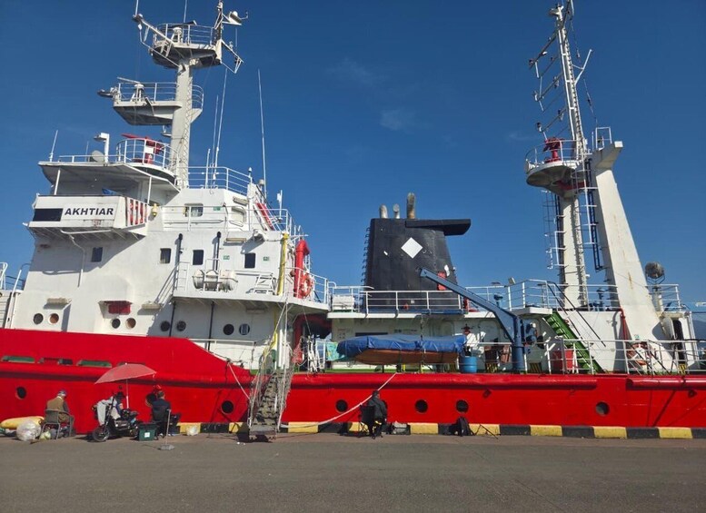A large ship named AKHTIAR docked at a port with several people and equipment around. 3