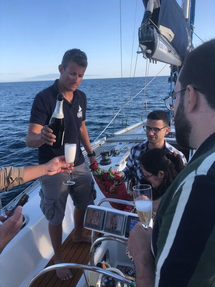 A group of people on a sailboat, holding drinks and a bouquet of flowers. 5
