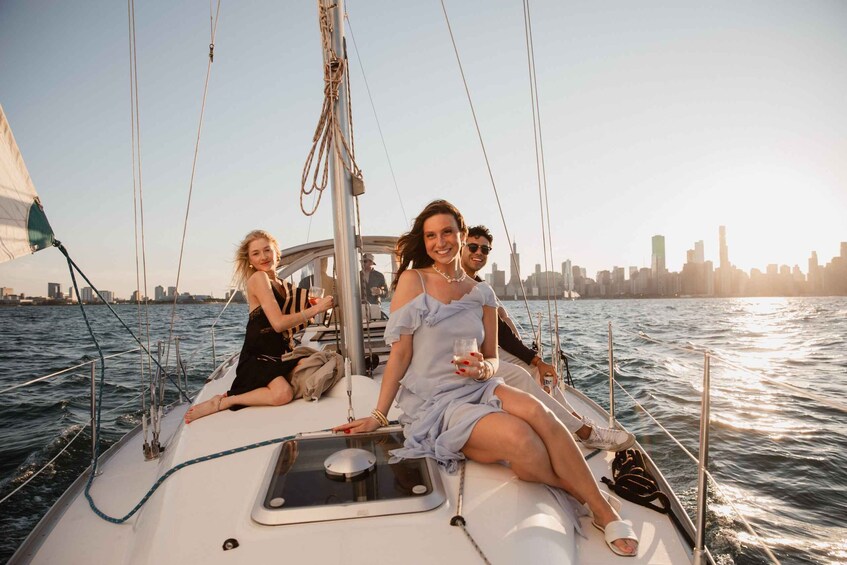 A sailboat with three people on board, a city skyline in the background, and a clear sky. 1