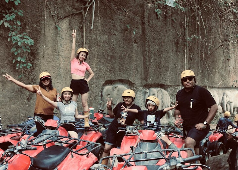 A group of people on ATVs with helmets, a rocky wall, and greenery in the background. 2