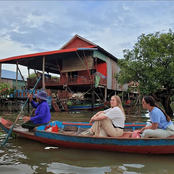 A group of people in a boat on a river, with a house on stilts in the background. 5