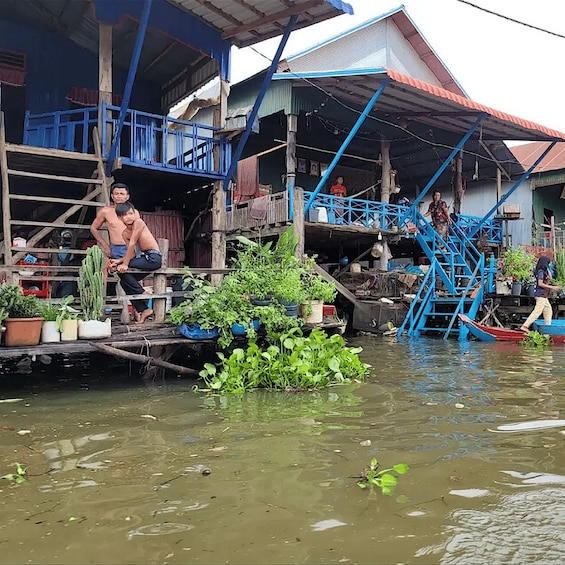 A floating house with blue railings and stairs leading to the roof, surrounded by water with plants and debris. 2