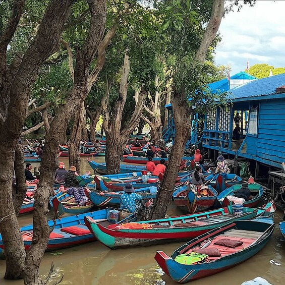 A river with boats docked under trees, a blue building, and people on the boats. 4