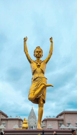 A golden statue of a figure with raised arms, standing on a platform with a temple in the background. 5