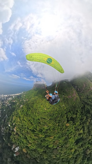 Un parapendio con una volta verde che vola sopra una zona montuosa ricca di vegetazione e una città costiera sullo sfondo. 1
