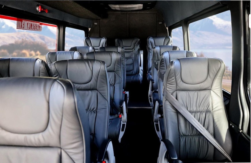 The interior of a vehicle with multiple rows of seats, a rearview mirror, and a window with a view of a mountainous landscape. 3