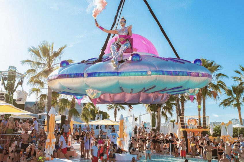 A person in a costume on a large inflatable structure above a crowded pool area. 4