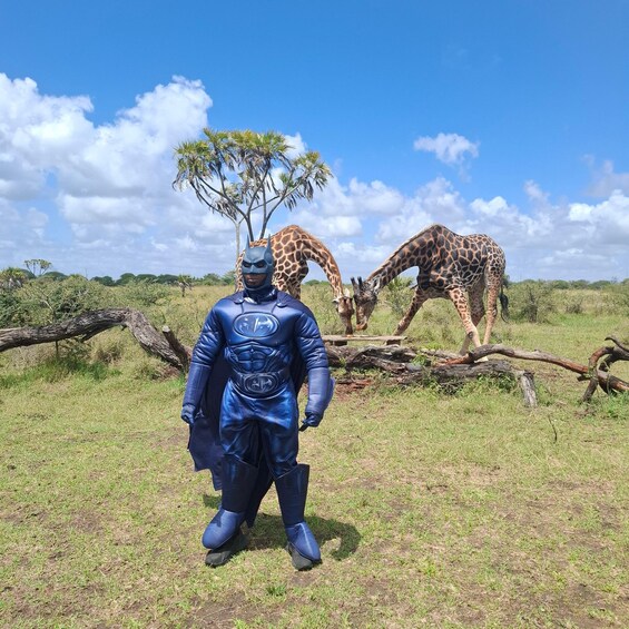A person in a blue costume standing in a grassy field with giraffes in the background. 5