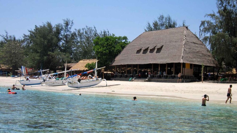 A beach with thatched-roof structures, clear shallow waters, and several boats. 4