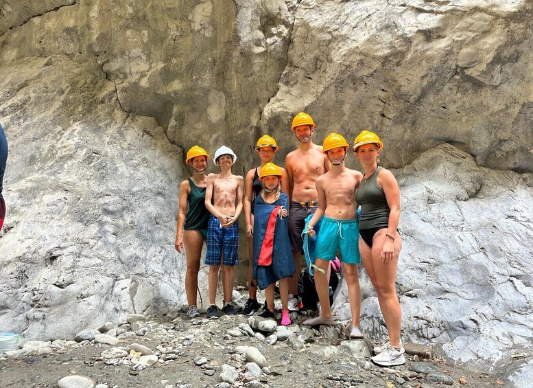 A group of people wearing safety helmets standing in front of a rocky cliff. 3