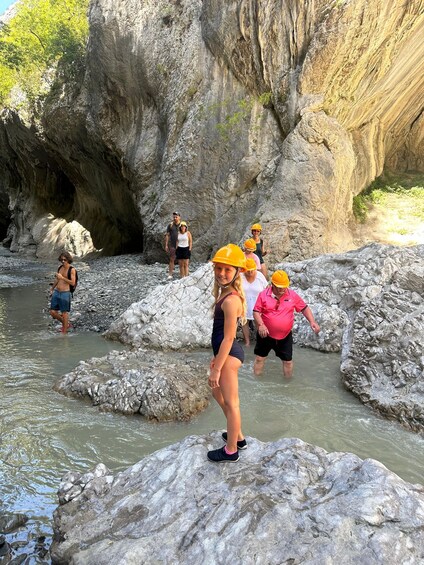 A group of people wearing helmets and standing on rocks by a river. 1