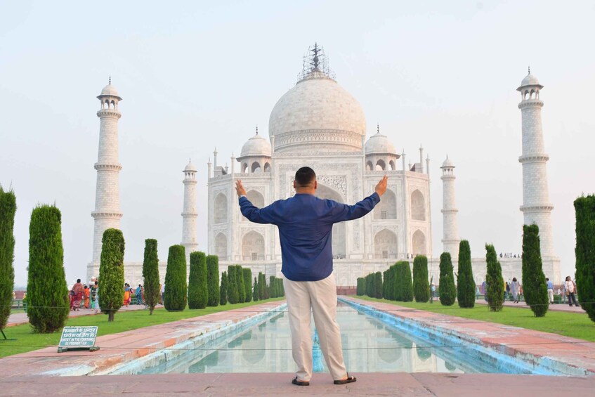 A person standing in front of the Taj Mahal with arms raised, surrounded by manicured trees and a reflecting pool. 5