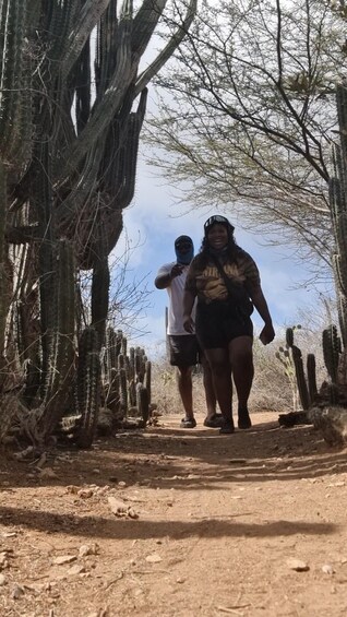 Un sentier de terre bordé de cactus et d’arbres, sur lequel marchent deux personnes. 5