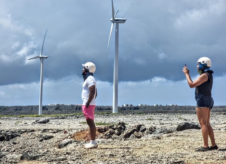 Two people standing on a rocky terrain with wind turbines in the background. 1