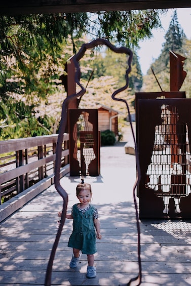 A child in a green dress standing on a wooden bridge with a metal sculpture of a woman in the background. 5