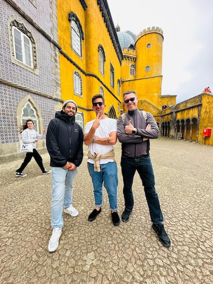 Three people standing in front of a yellow building with a tower. 4