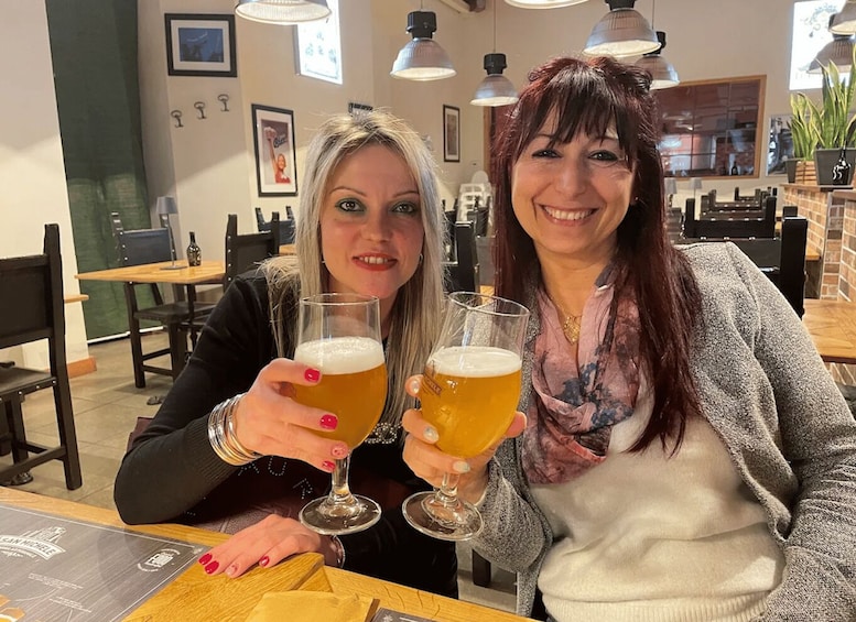Two people toasting with beer glasses in a restaurant with hanging lights and framed pictures on the wall. 4
