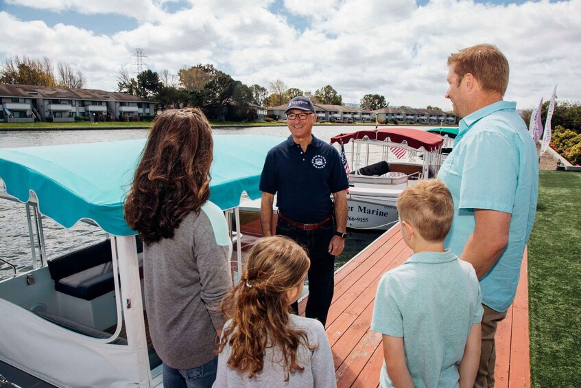 A group of people on a boat docked near a marina with a building in the background. 1