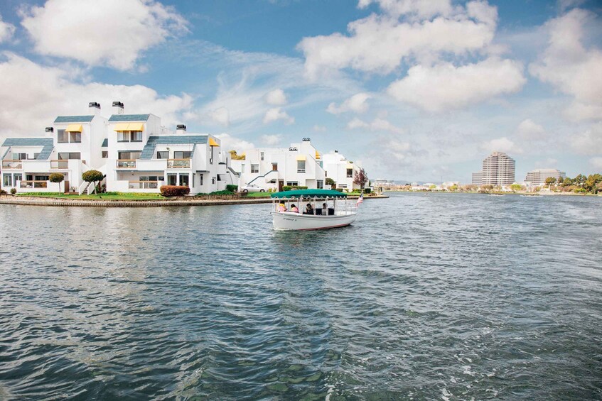 A waterfront with modern white buildings, a boat on the water, and distant high-rise buildings. 3