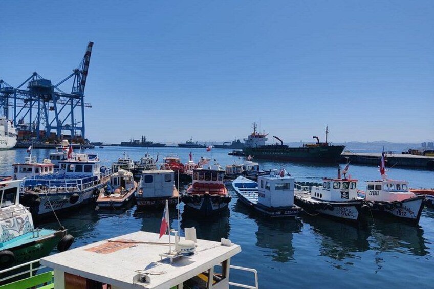 Ein Hafen mit mehreren vertäuten Booten, ein großes Schiff im Hintergrund und ein Kran. 2
