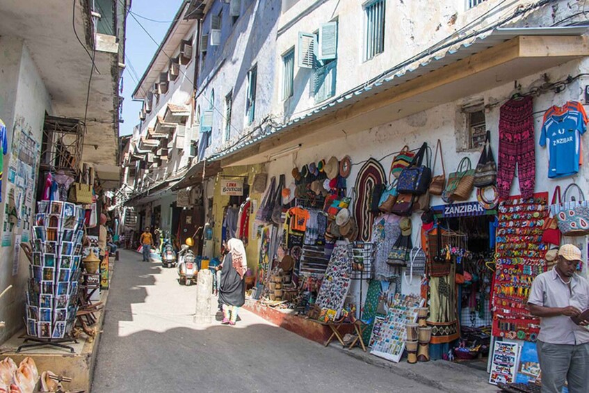 A narrow street with shops on both sides selling hats, bags, and clothing. 5