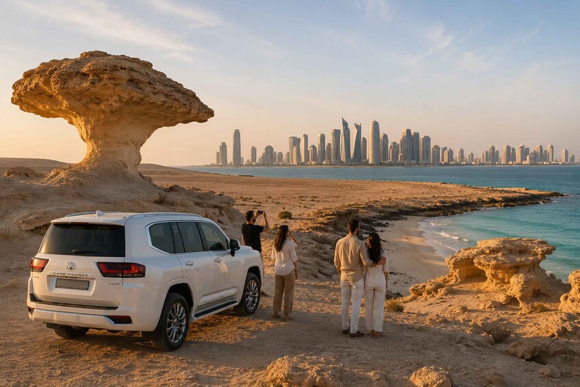 A white SUV parked on a sandy beach with a rocky formation in the foreground and a city skyline in the background. 1