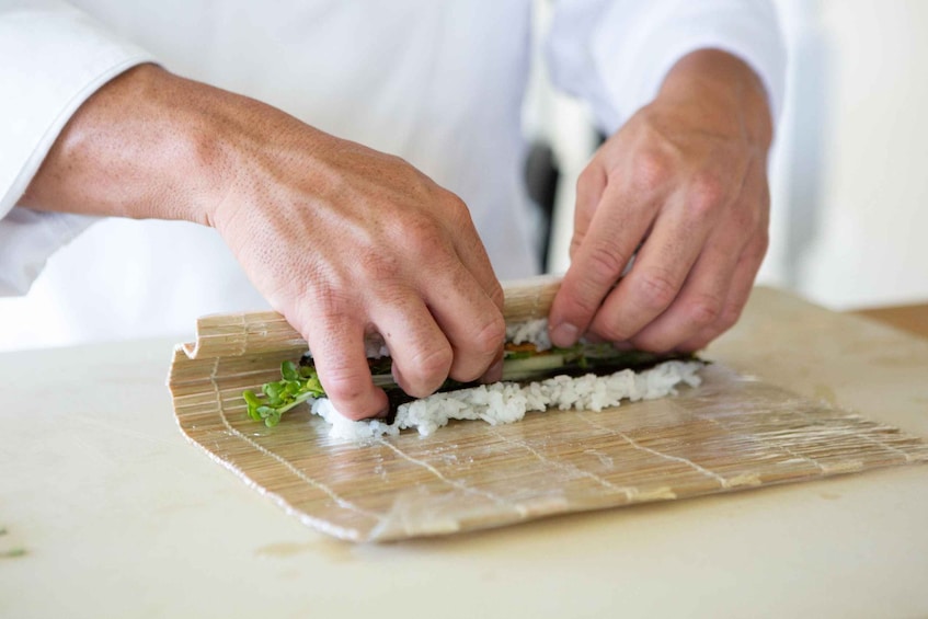 A person preparing sushi on a bamboo mat. 3
