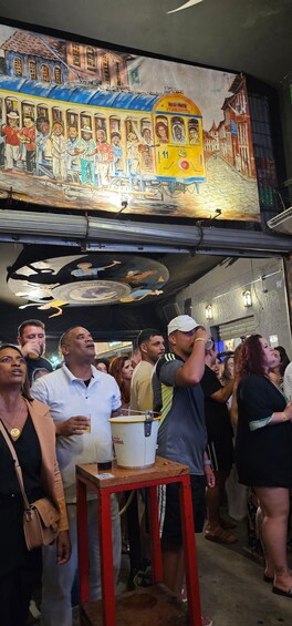 A mural of a colorful tram and people, a crowd of people, and a bucket on a table. 2