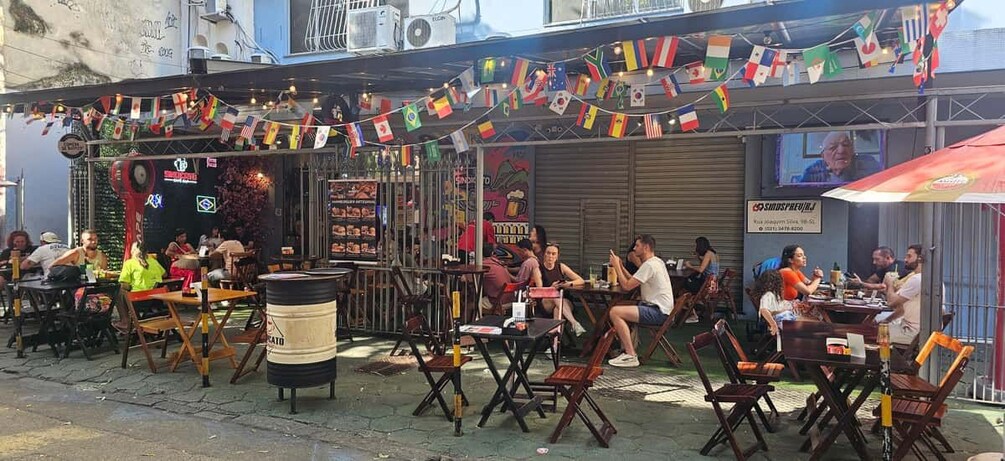 An outdoor café with tables and chairs, flags, and a signboard. 3