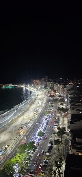 A nighttime coastal cityscape with a beach, a busy road, and high-rise buildings. 5