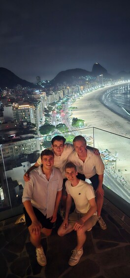 A group of people posing on a balcony overlooking a brightly lit beach at night. 5