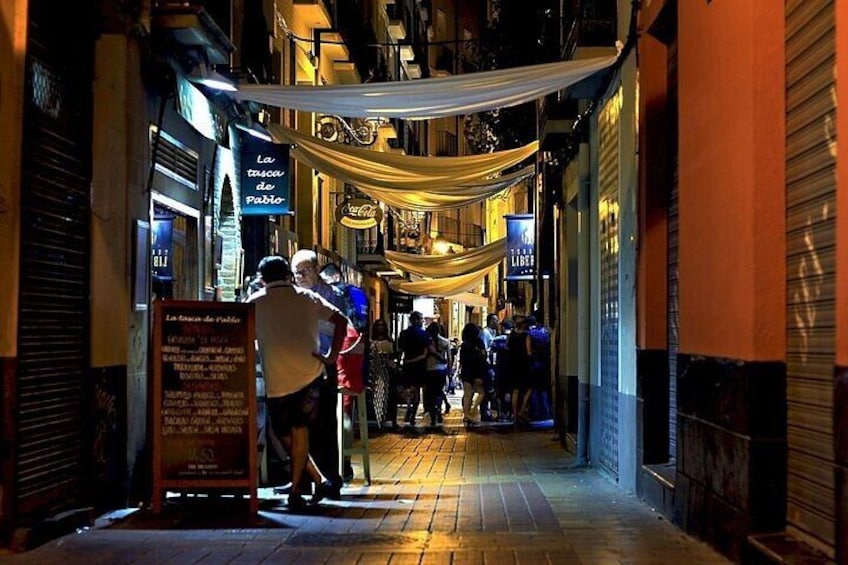 A narrow street with people walking, shops with closed shutters, and a signboard. 5