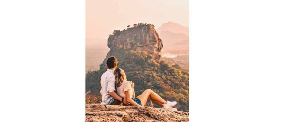 A couple sitting on a rocky outcrop overlooking a mountainous landscape with a prominent rock formation. 5