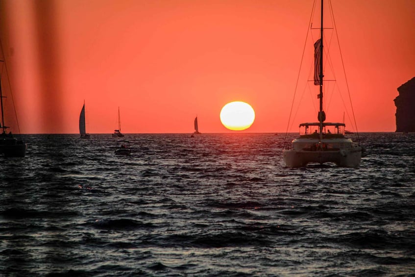 A sunset over the ocean with sailboats and a small boat. 1
