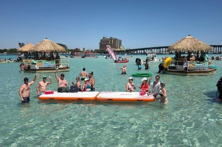 A group of people on a floating platform in clear water, with a thatched-roof structure and a pier in the background. 2