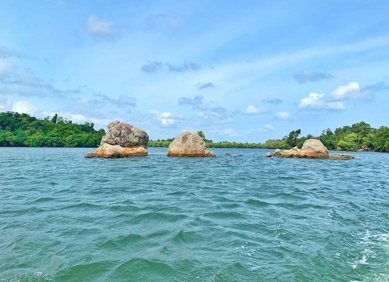 Three large rocks in a body of water with a forested shoreline and a partly cloudy sky. 2