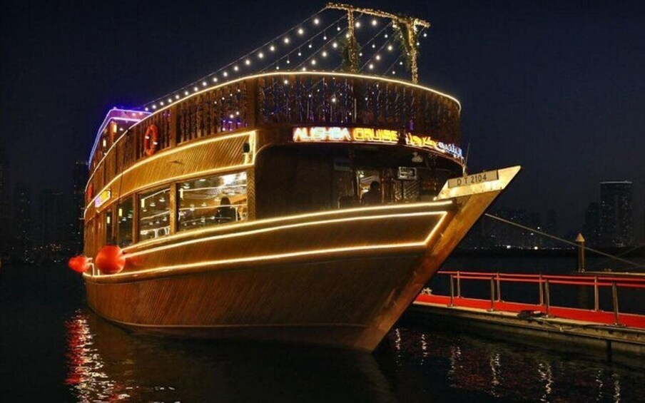 A large, illuminated boat with a wooden exterior and a bridge structure on top, docked at night. 3