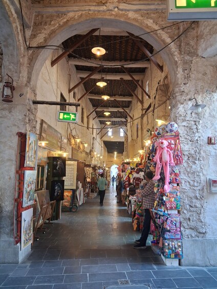 An indoor market with stone walls, hanging lights, and various stalls selling toys and art. 5