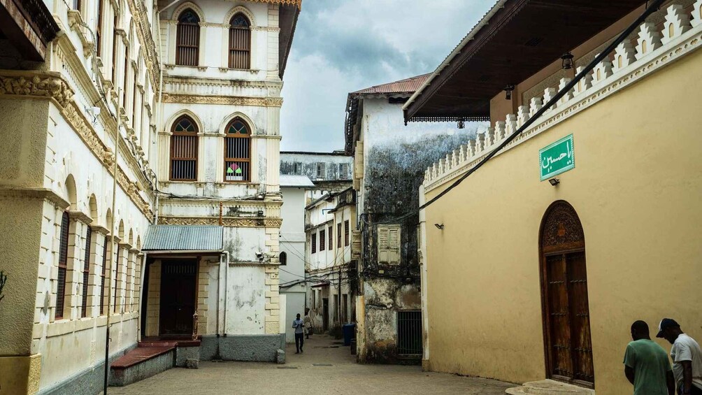A narrow alleyway between historic buildings with ornate facades and a green street sign. 2