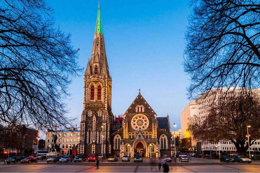 A Gothic-style church with a tall spire and a large circular window, surrounded by modern buildings and leafless trees. 2