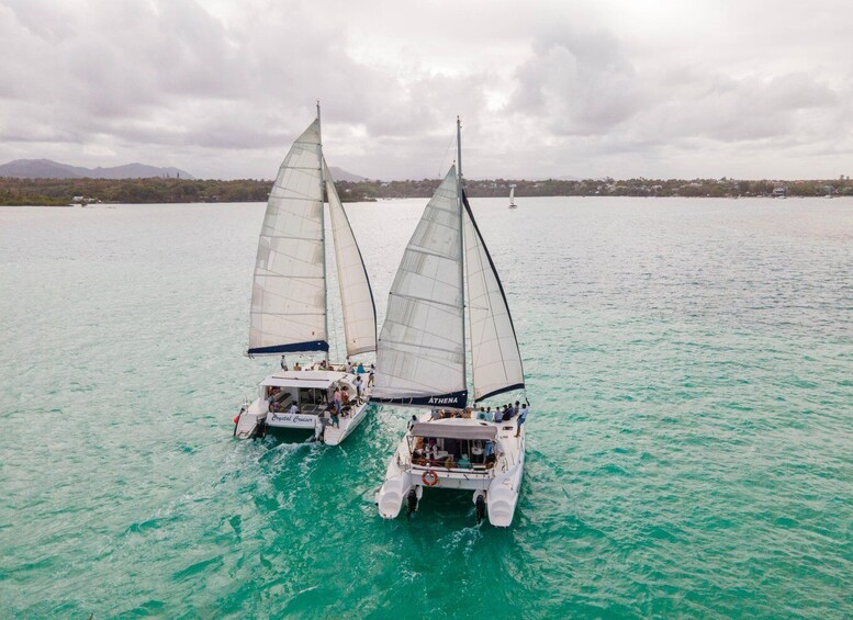 Two sailboats named ATHENA on turquoise waters with a mountainous landscape in the background. 2