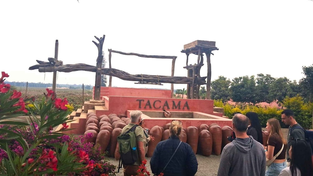 A wooden structure with the word 'TACAMA' on it, surrounded by visitors and colorful flowers. 5