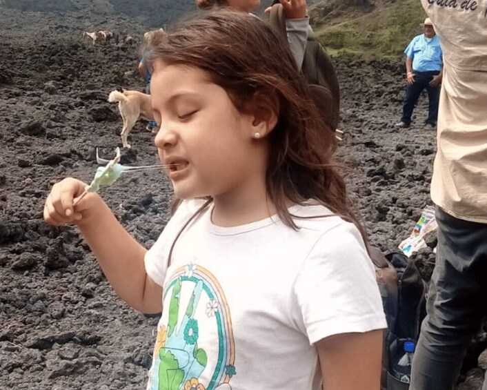 A child holding a green object, standing on a volcanic terrain with people in the background. 2