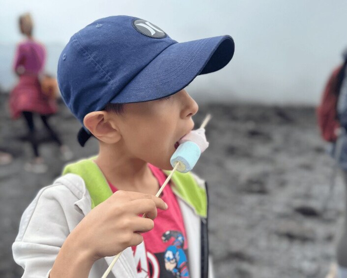 A child wearing a blue cap and a white jacket with a green hood, holding a lollipop. 1