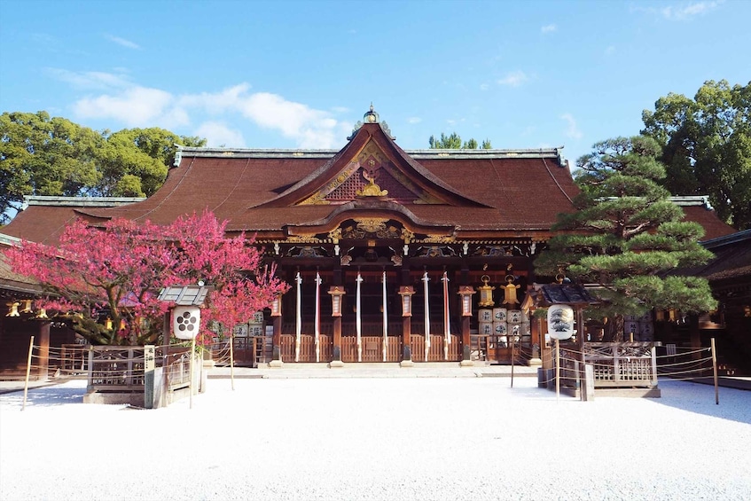A traditional Japanese temple with a red roof, wooden pillars, and a cherry blossom tree in the foreground. 1