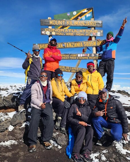 A group of people at the summit of Mount Kilimanjaro, with a sign indicating the highest point in Tanzania. 5