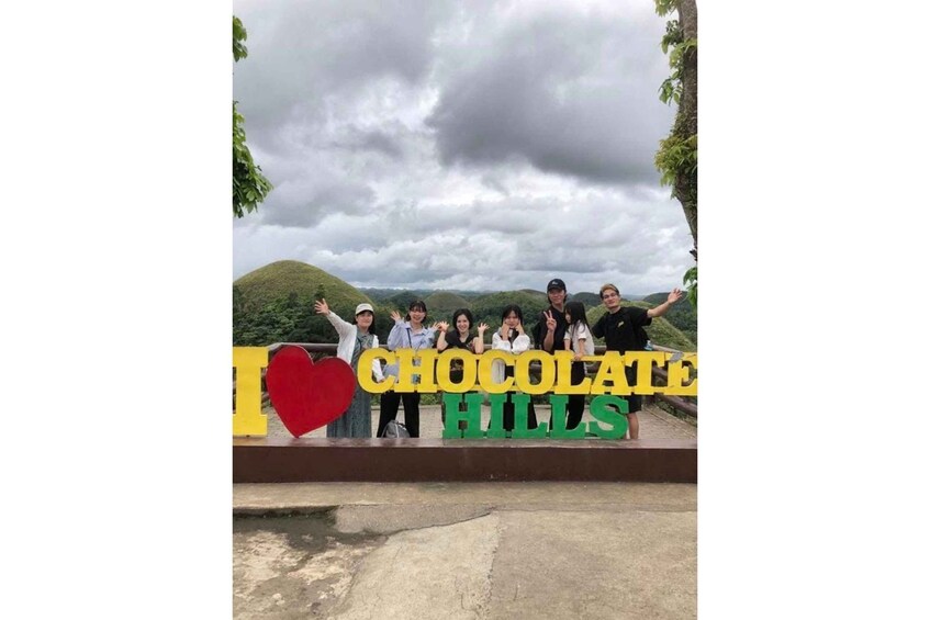 A group of people posing in front of a sign that reads "I ♥ CHOCOLATE HILLS". 1