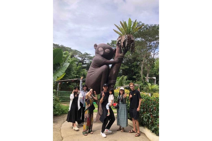 A group of people posing with a large statue of a bear holding a tree. 4