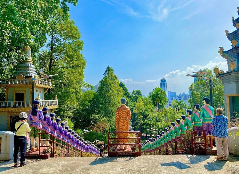 A statue of a monk in orange robes surrounded by rows of colorful statues. 1