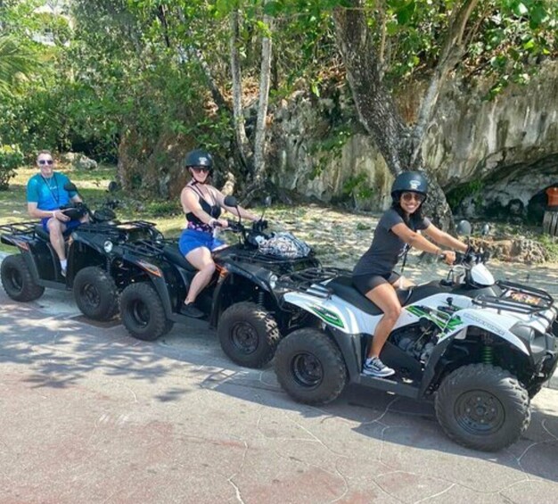 Three people riding ATVs on a paved path surrounded by trees and rocks. 1